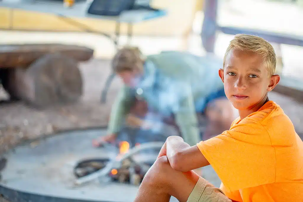 A teenage boy relaxes while a staff builds a fire in the background | ThreePeaks Ascent Residential Treatment Center